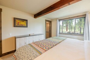 Ein Schlafzimmer mit einem großen Bett, einem Fenster mit Blick auf einen Wald, einem Holzbalken an der Decke und einem gerahmten Bild an der Wand.