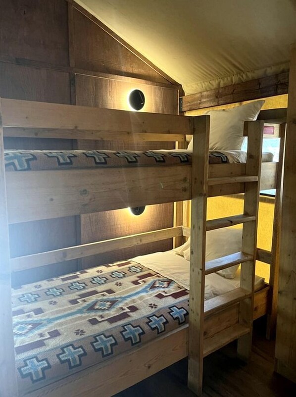 Una cama litera con un edredón estampado, cabecera de madera y una lámpara con forma circular.