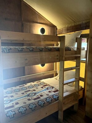 Ein Stockbett mit gemustertem Bettbezug, einem Holzkopfteil und einer runden Leuchte.