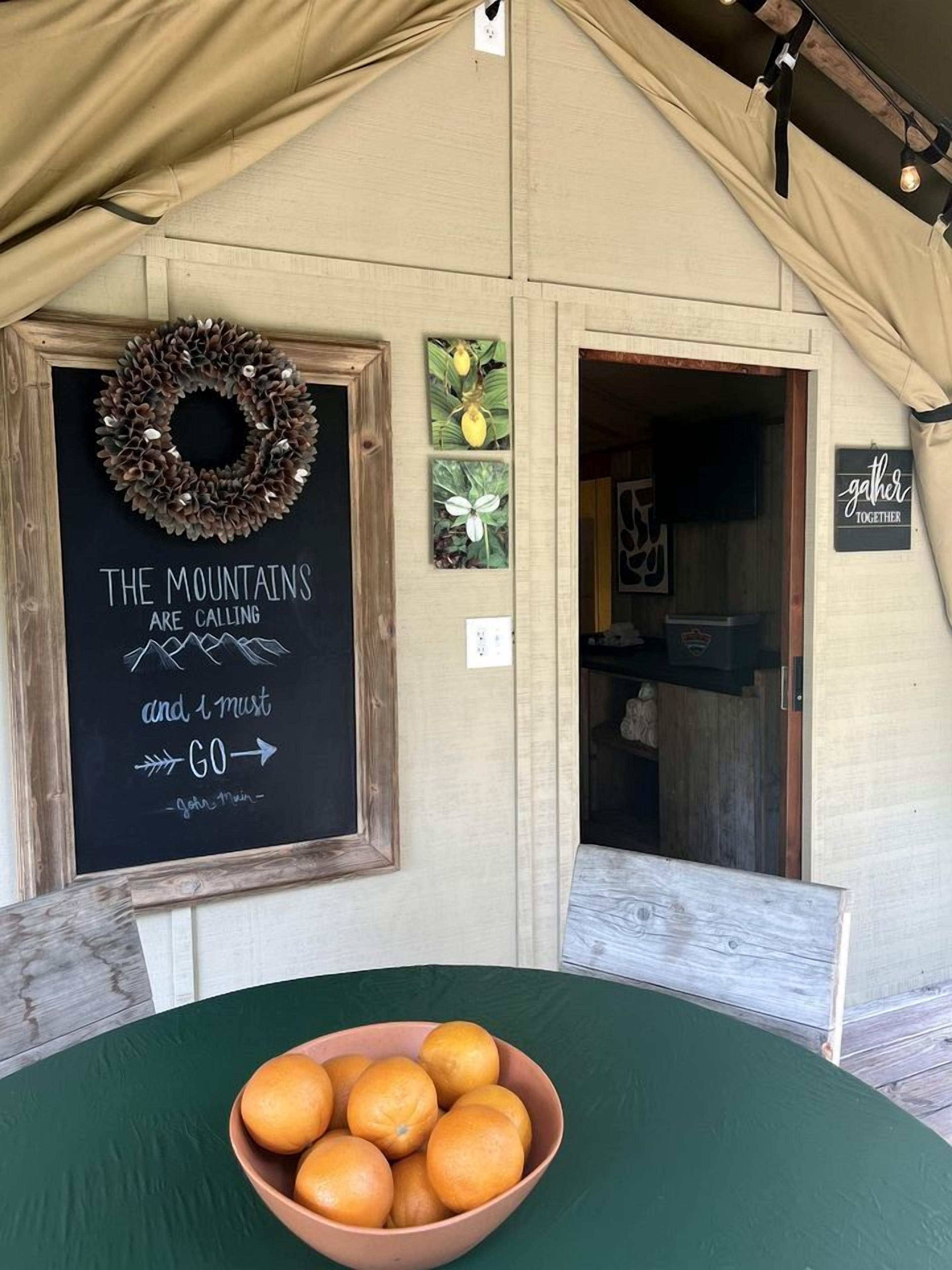 Interior rústico com um quadro negro, uma porta de madeira e uma mesa com laranjas.
