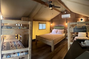 Ein rustikaler Holzraum mit Etagenbetten, einem zentralen Bett und einem kleinen Tisch mit einem Schild.
