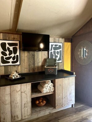 Un espace bar avec un comptoir en bois, un téléviseur fixé au mur au-dessus, et des œuvres d’art accrochées aux murs.
