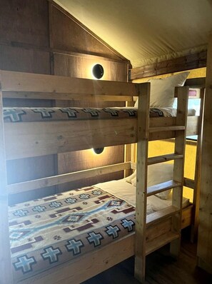 Una cama litera con un edredón estampado, cabecera de madera y una lámpara con forma circular.