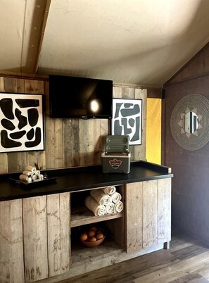 A wooden bar area with a television, a decorative mirror, and a shelf with rolled towels.