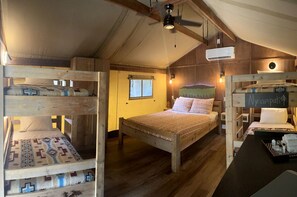 Une pièce rustique en bois, avec des lits superposés, un lit principal et une petite table sur laquelle est posé un panneau.