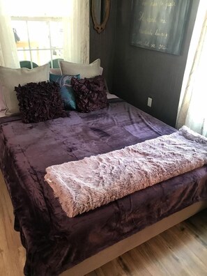 A bed with a purple bedspread, decorative pillows, and a fluffy blanket.