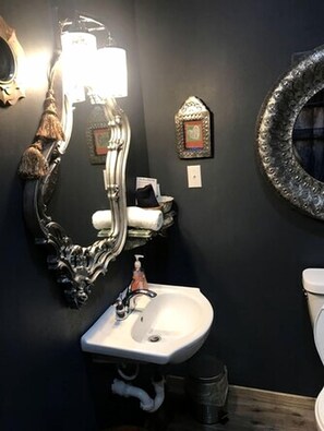 A bathroom with a large ornate mirror, a white sink, a toilet, and a decorative wall piece.