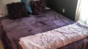 Ein Bett mit einer violetten Tagesdecke, dekorativen Kissen und einer flauschigen Decke.