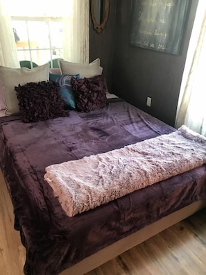 Ein Bett mit einer violetten Tagesdecke, dekorativen Kissen und einer flauschigen Decke.
