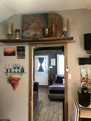 A doorway leading to a room with a bed, a coffee machine, and a shelf with decorative items.