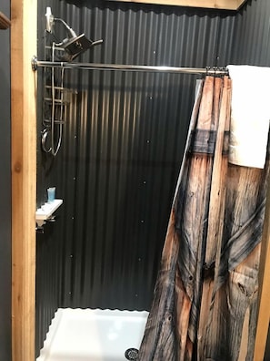Ein Duschbereich mit Duschkopf aus Metall, einem weißen Waschbecken und einem Duschvorhang aus Holz.