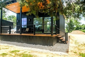 A modern building with a wooden deck, outdoor seating, and large windows.