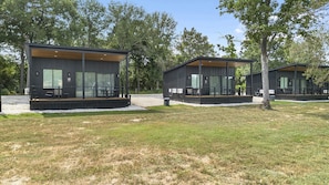 Two modern cabins with large windows, wooden decks, and a grassy area.