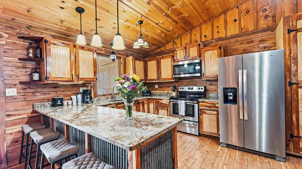 A kitchen with wooden cabinets, a stainless steel refrigerator, a granite countertop, and bar stools.