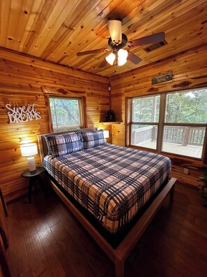 Een slaapkamer in een houten hut met een bed, een plafondventilator en een bordje met de tekst 'Sweet Dreams'.