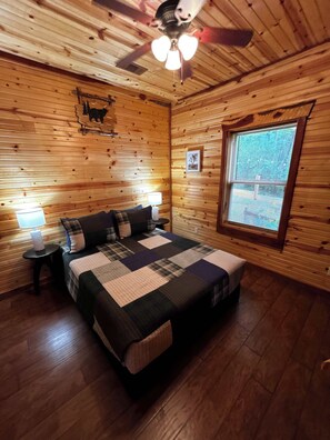 A wooden-paneled room with a bed, a ceiling fan, a window, and a wall-mounted picture. - Hot Tub, Pool Table, Sunset Views (Eureka Springs)