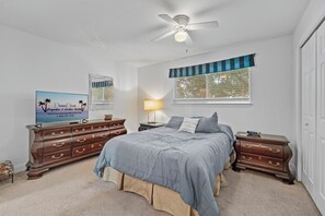 Ein Schlafzimmer mit Bett, Schminktisch, Nachttisch, Lampe und einem Fernseher, der 'DunnDeal Properties & Vacation Rentals' anzeigt.