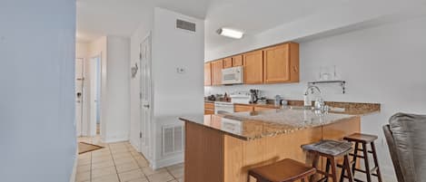 A kitchen with wooden cabinets, a microwave, a sink, and a bar area with stools.