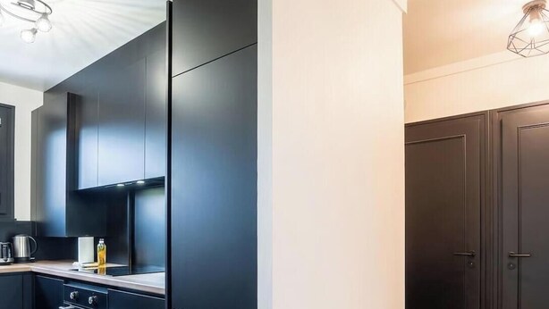 A modern kitchen with dark cabinetry, a built-in oven, and a countertop with a kettle and a bottle. - Chez Lionel I T4 I Annemasse (Annemasse)