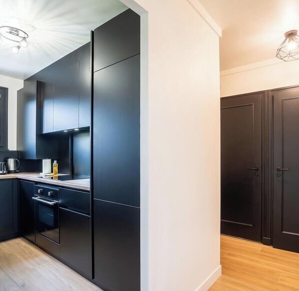 A modern kitchen with dark cabinetry, a built-in oven, and a countertop with a kettle and a bottle.