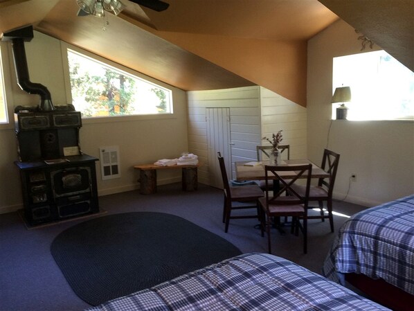 A room with a fireplace, a dining table with chairs, a window, and two beds.