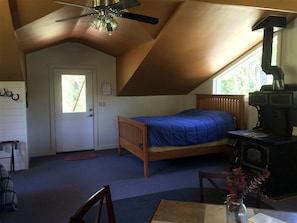 A bedroom with a bed, a wooden dresser, a ceiling fan, a window, and a fireplace.