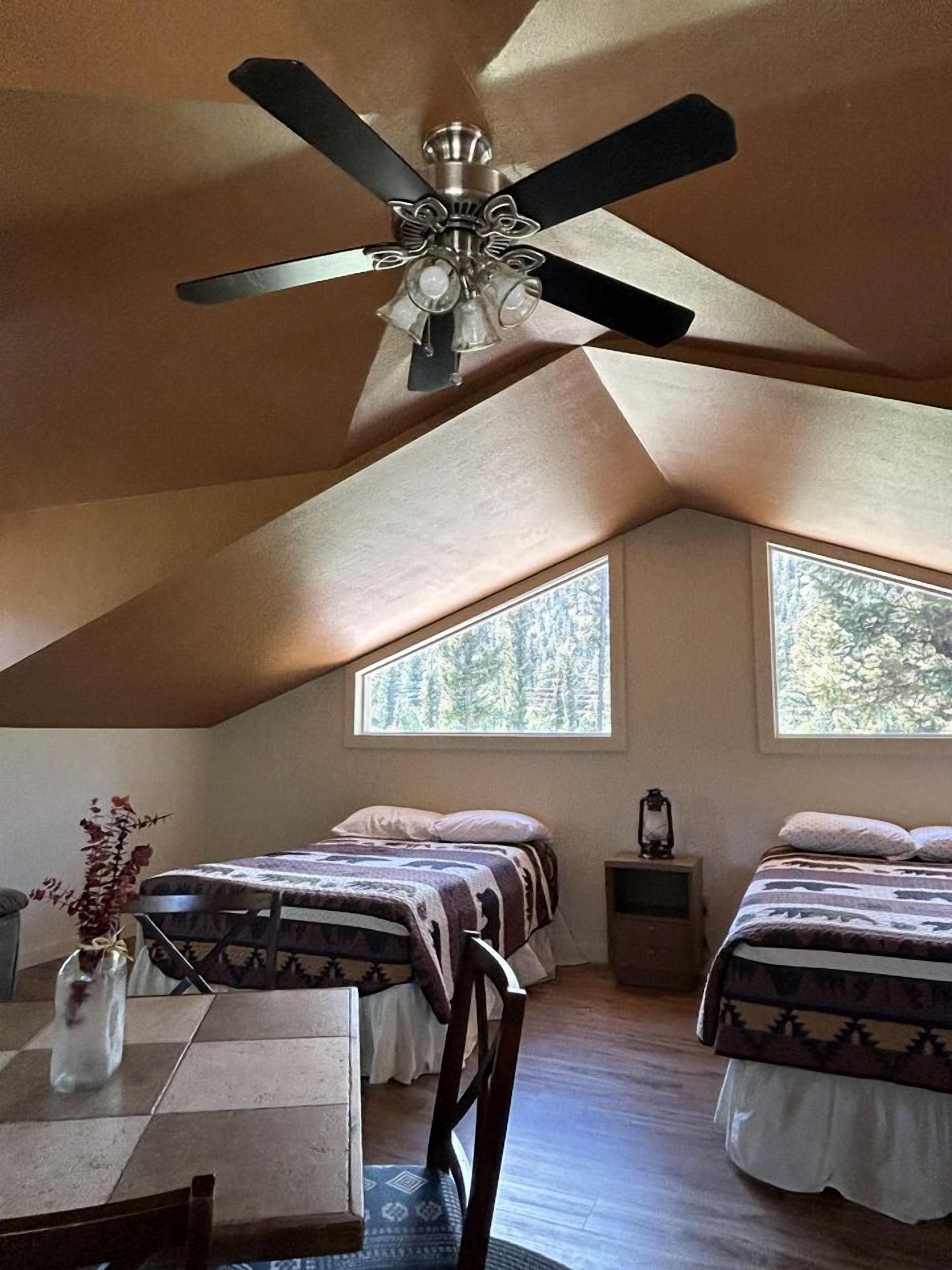 A bedroom with two beds, a ceiling fan, and large windows.