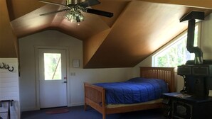 A bedroom with a bed, a wooden dresser, a ceiling fan, a window, and a fireplace. - Charming Loft-Style Cabin Rental for Six near Missoula, Montana (Hall)