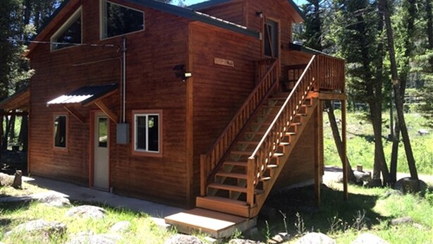 A two-story wooden cabin with a staircase, a front door, and a small porch area. - Charming Loft-Style Cabin Rental for Six near Missoula, Montana (Hall)