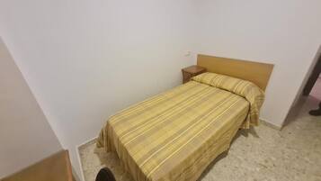 A single bed with a wooden headboard and a matching pillow in a room with white walls and a tiled floor.