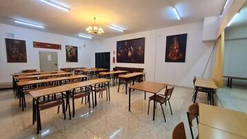 Un aula con escritorios y sillas de madera, una araña y arte religioso en las paredes.