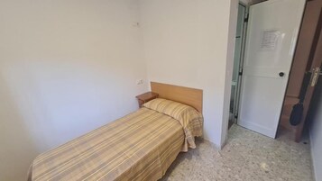 Una habitación pequeña con cama individual, cabecera de madera, mesita de noche y puerta que da a un baño.