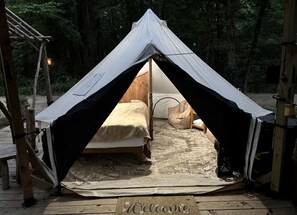 A tent with a bed inside, a welcome mat, and a wooden deck.