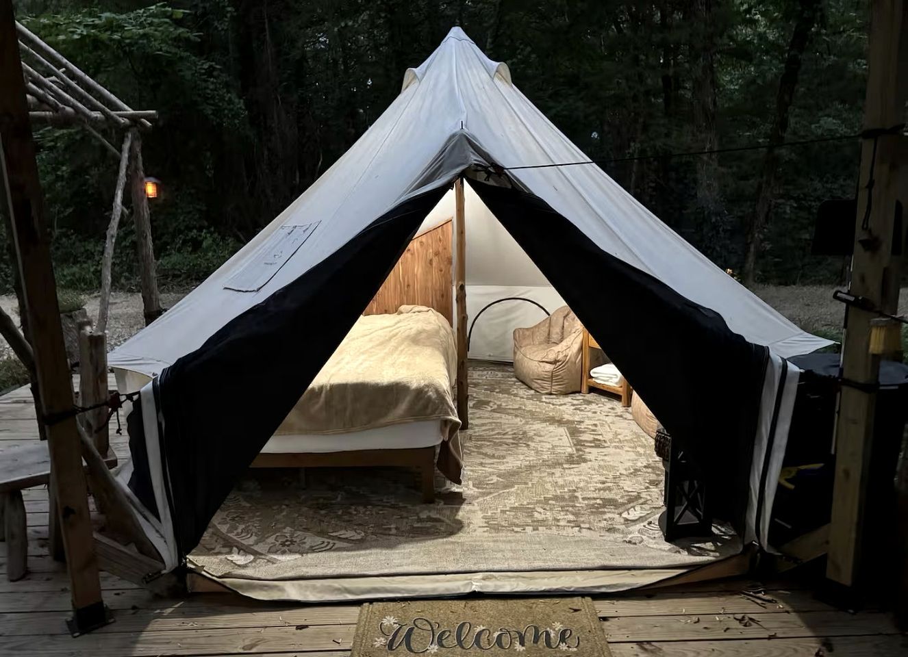 A tent with a bed inside, a welcome mat, and a wooden deck.