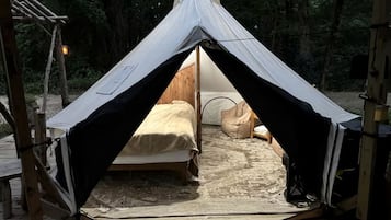 A tent with a bed inside, a welcome mat, and a wooden deck.