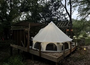 A tent with a wooden deck, surrounded by trees.