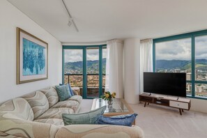 Ein modernes Wohnzimmer mit Sofa, Couchtisch, Fernseher und großen Fenstern mit Blick auf die Stadt.