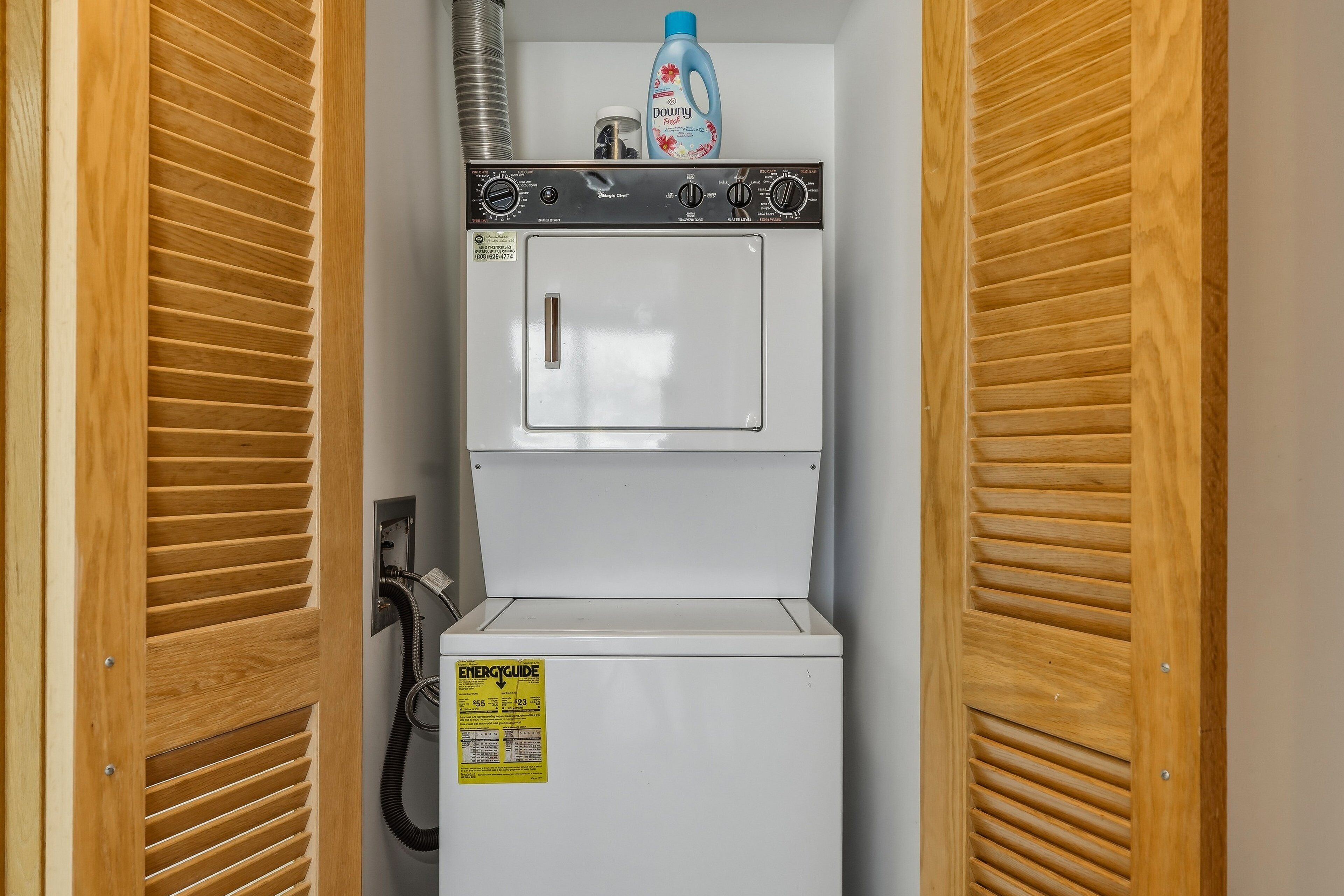 A compact laundry room with a front-loading washer and dryer, a water heater, and a power outlet.