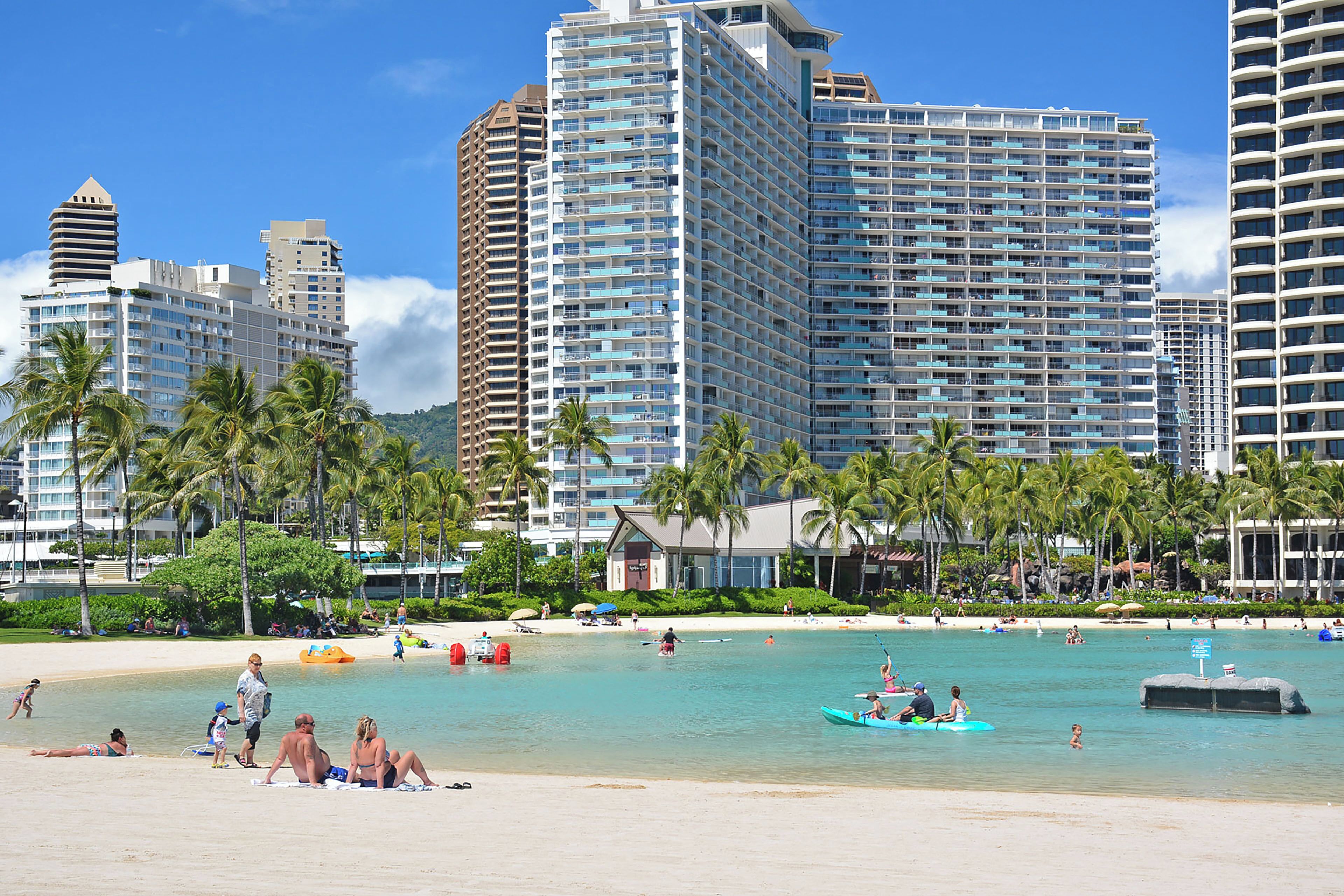 A beachfront hotel with high-rise buildings, palm trees, and a sandy beach.