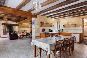 Une cuisine rustique avec des poutres en bois, un coin repas avec une table et des chaises, et une cheminée.