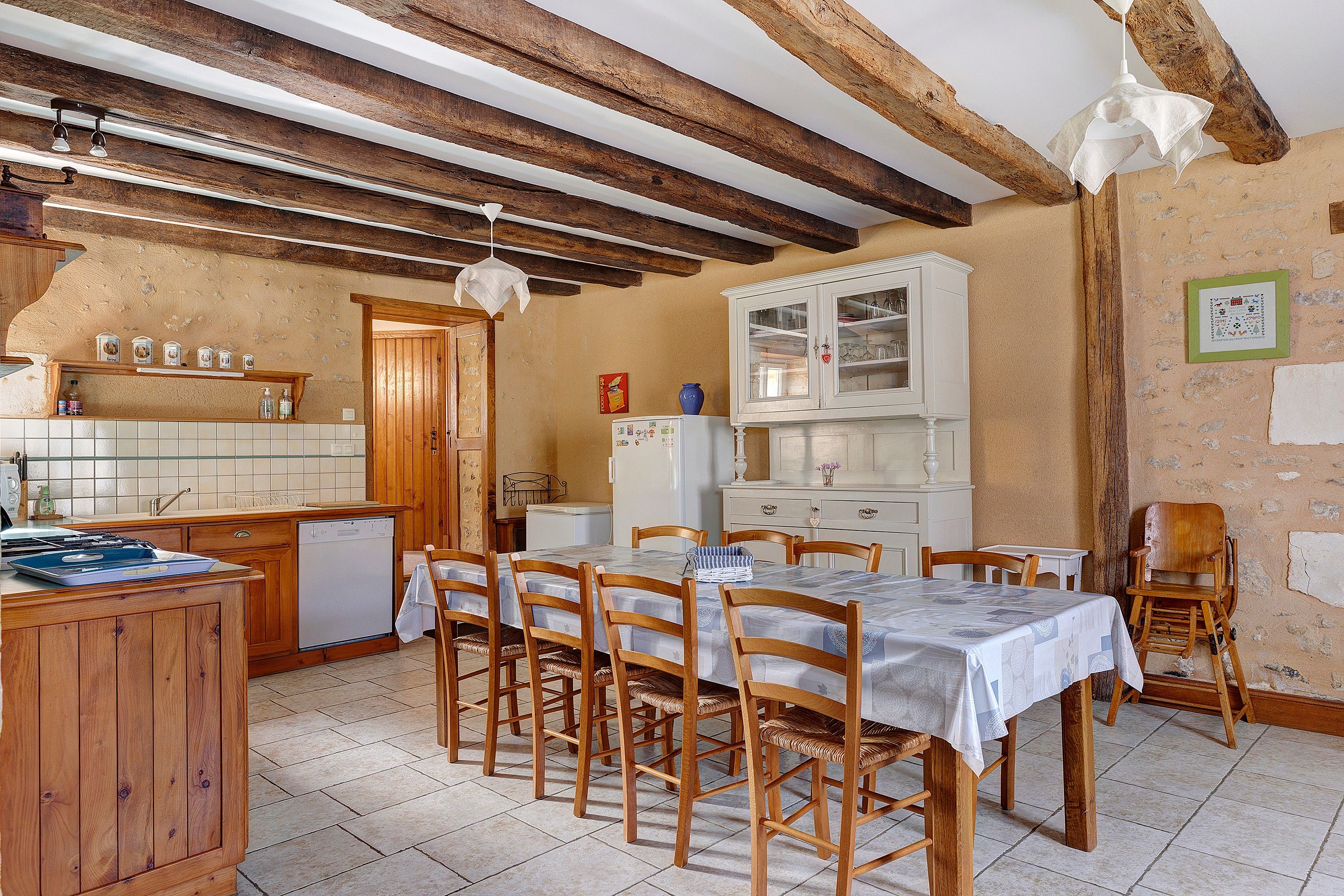 Une cuisine rustique avec des poutres en bois, un pare-feu en carreaux et un coin repas comprenant des chaises et une table en bois.