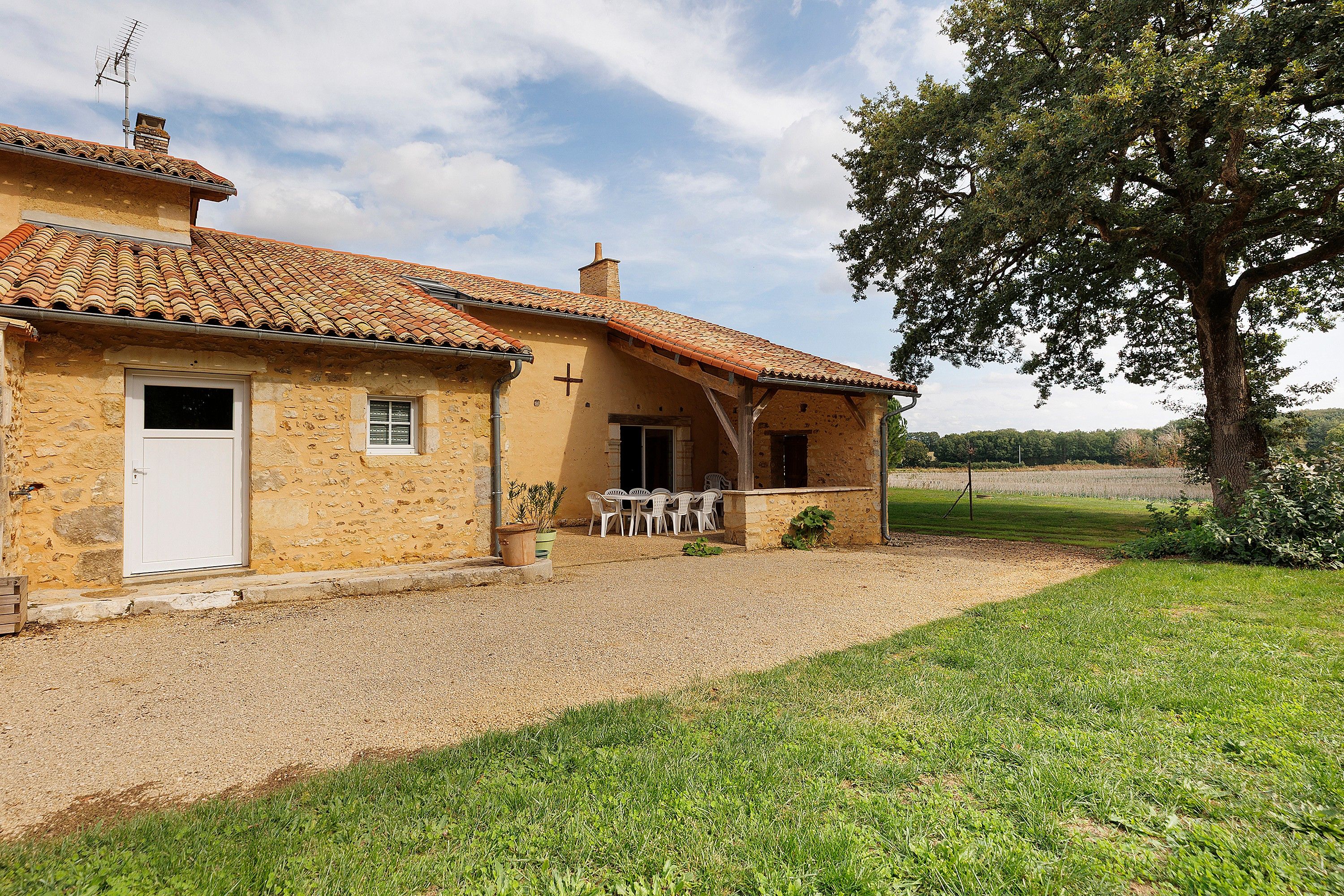 Un bâtiment rustique en pierre, doté d’un toit en tuiles, d’une porte et d’un petit porche avec des chaises.