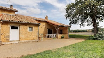 Un edificio rustico in pietra con tetto in tegole, una porta e un piccolo portico con sedie.