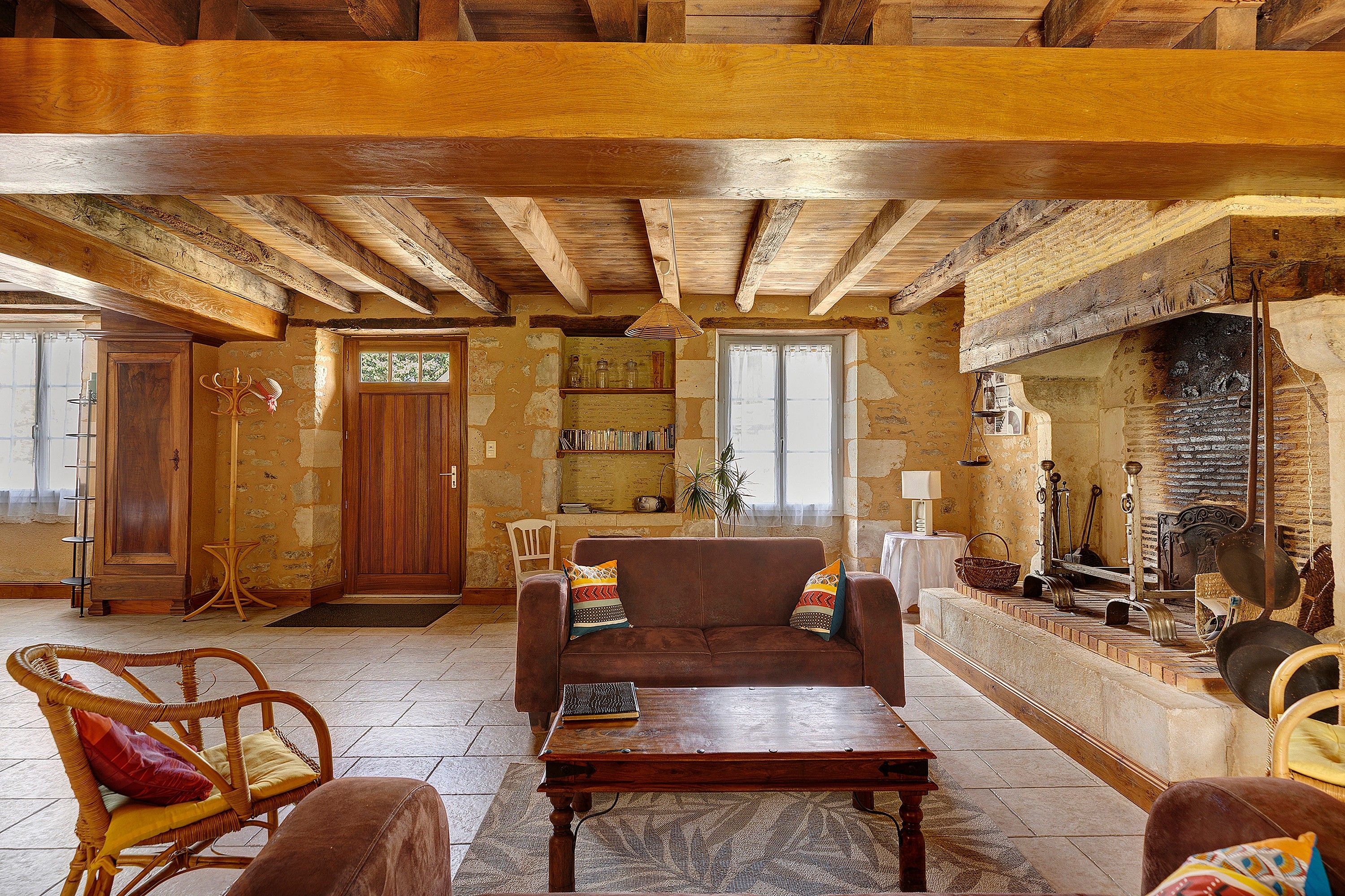 A rustic living room with exposed wooden beams, a fireplace, and a stone wall.