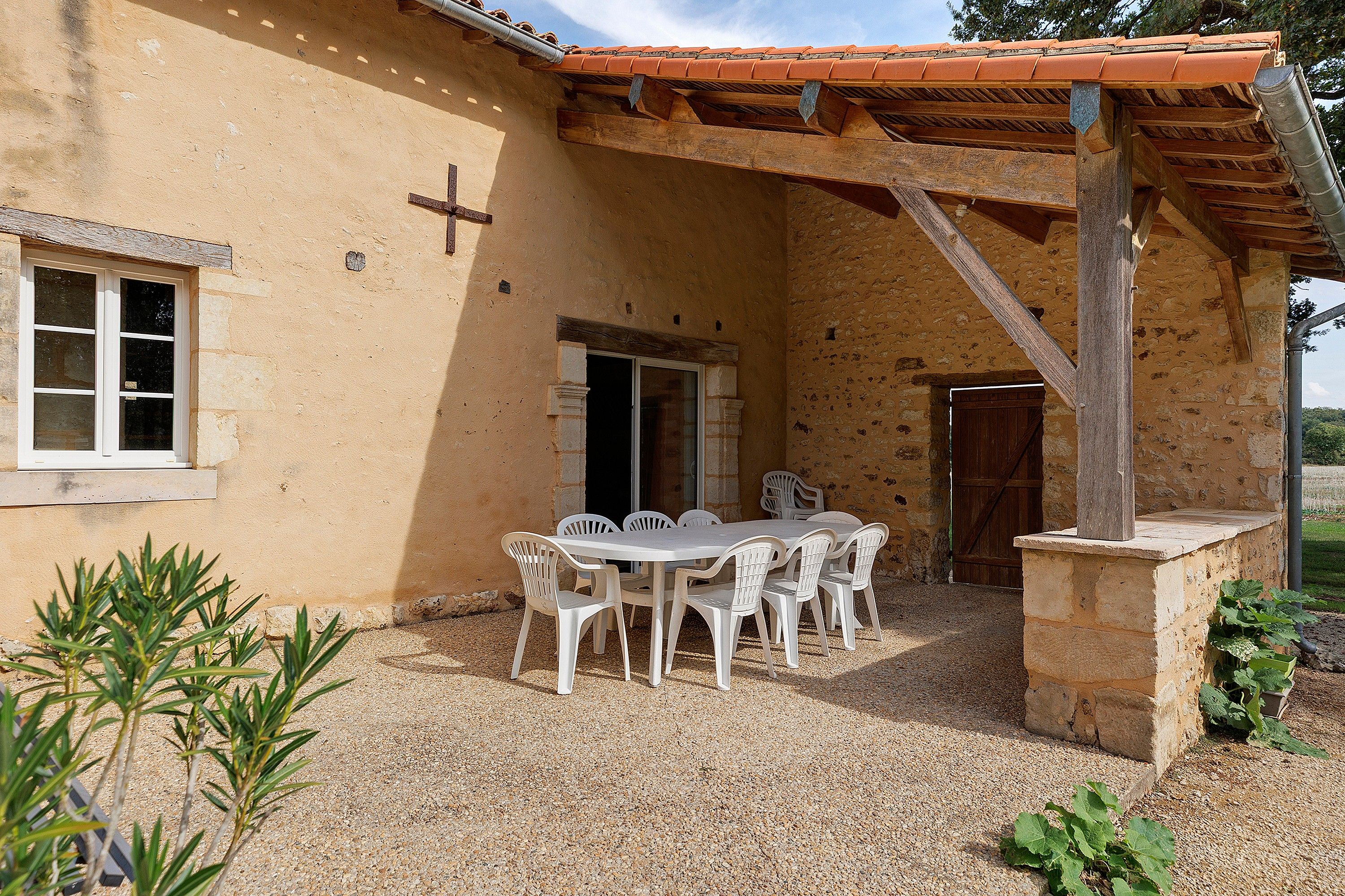 A rustic outdoor dining area with a table and chairs, a wooden pergola, and a stone wall.