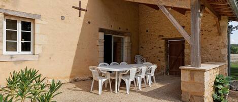 A rustic outdoor dining area with a table and chairs, a wooden pergola, and a stone wall.