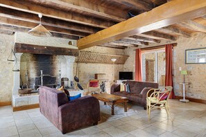A rustic living room with exposed wooden beams, a fireplace, a sofa, and a wicker chair. - Set of Holiday Homes - Swallows and Poultry (Lusignan)