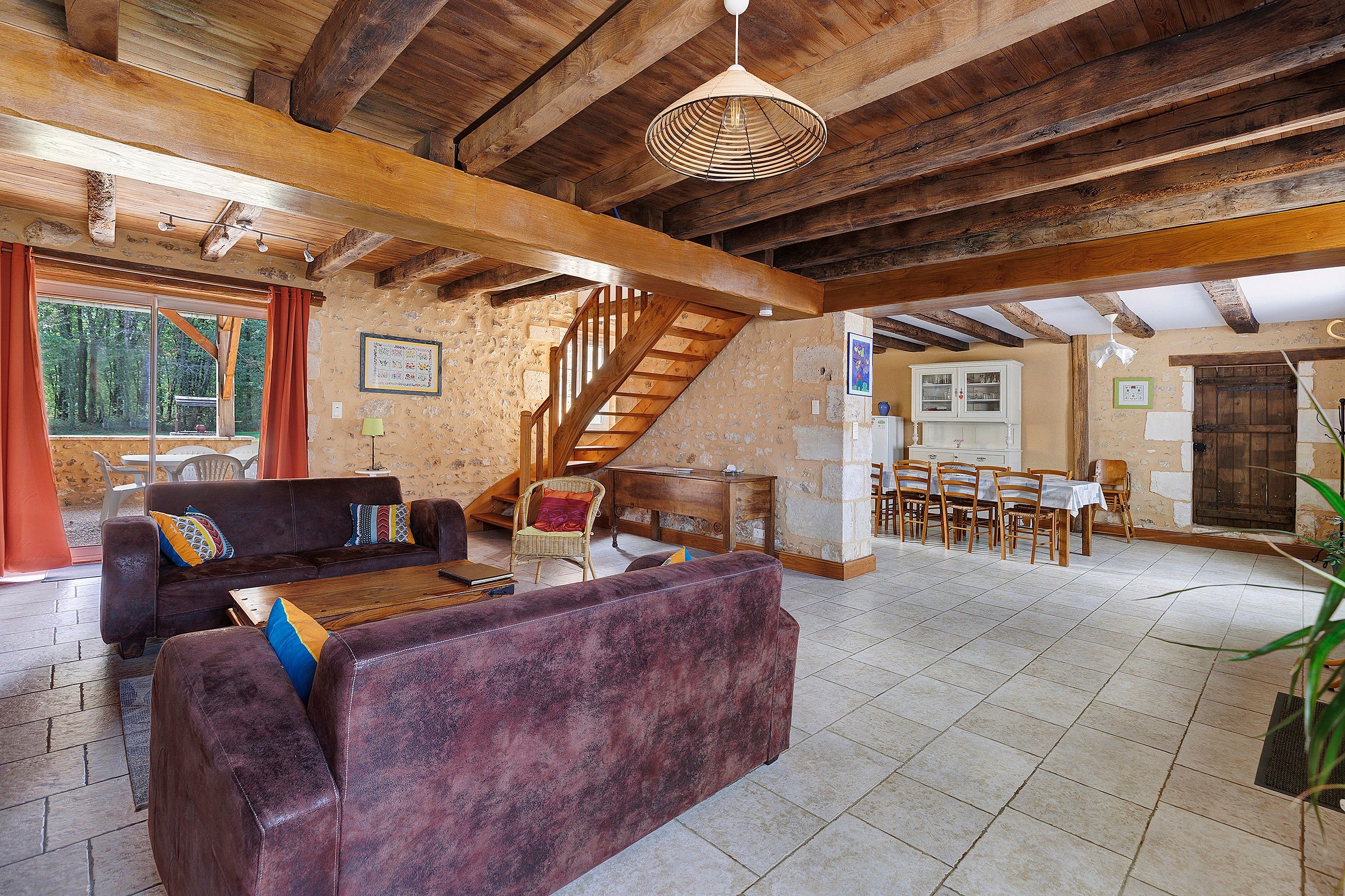 A rustic interior with a wooden staircase, a dining area, and a living room with sofas and a table.