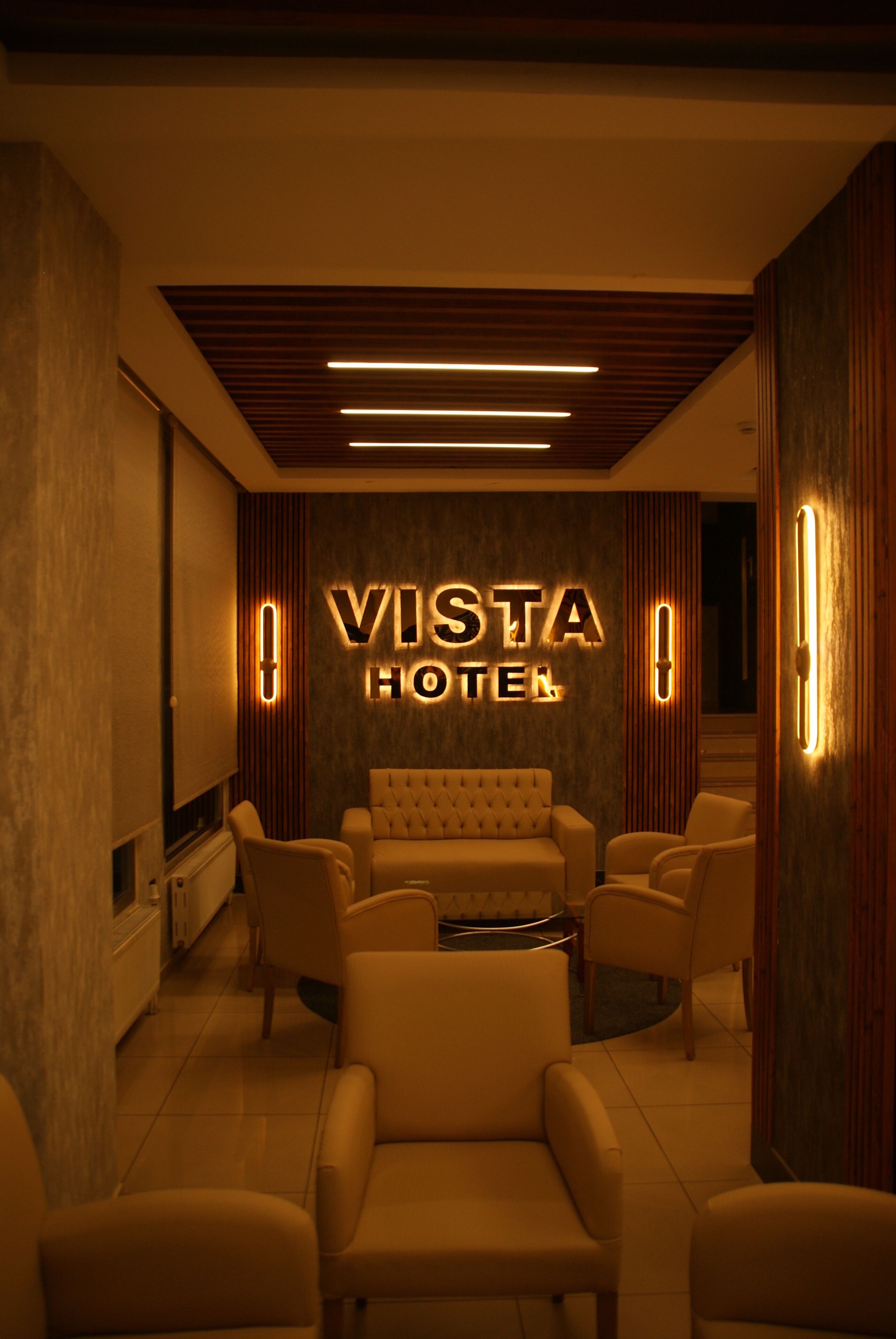 A hotel lobby with a 'VISTA HOTEL' sign, leather chairs, a sofa, and a wooden ceiling.