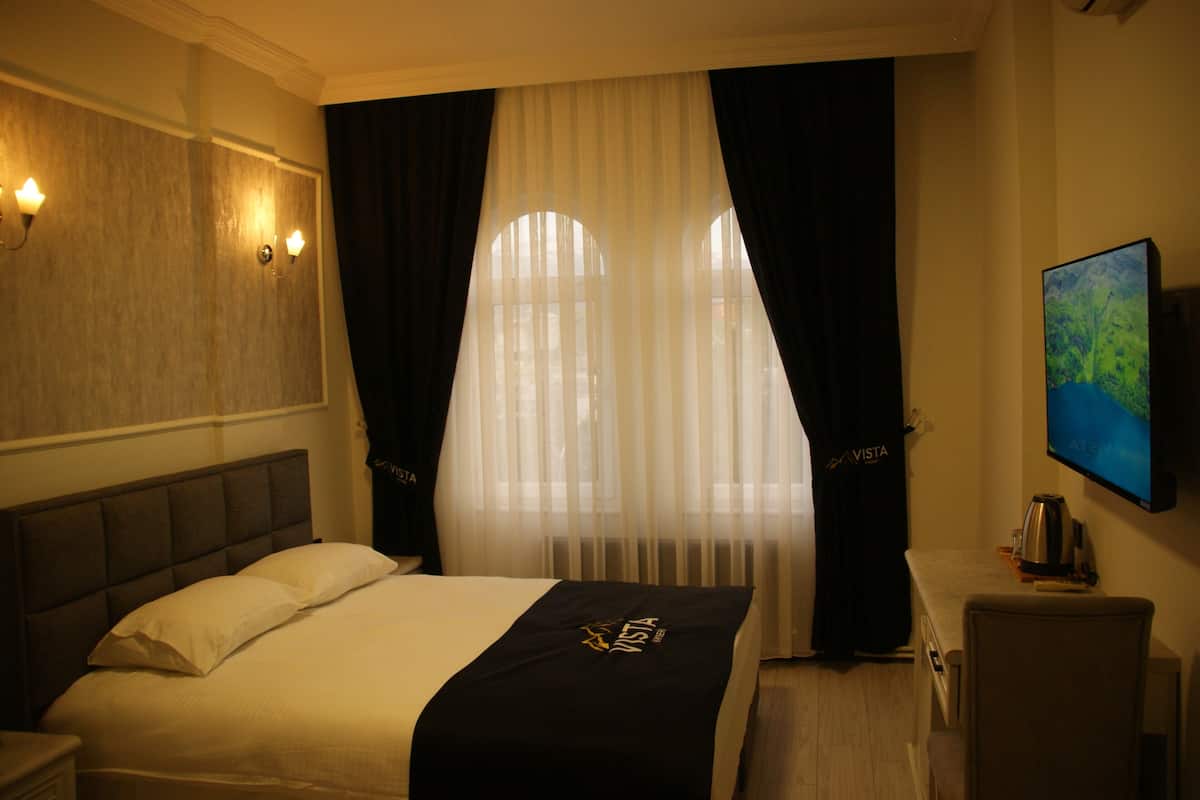 A hotel room with a bed, a nightstand, a desk, a chair, a television, and a window with curtains.